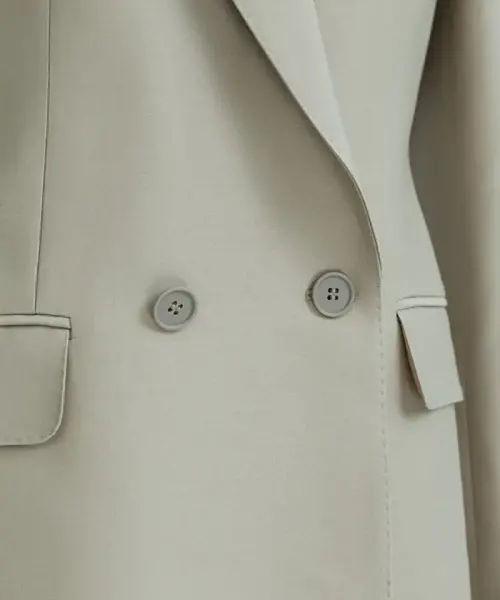 Ensemble beige Pure Élégance avec veste croisée à boutons et pantalon assorti, porté avec chemise claire.