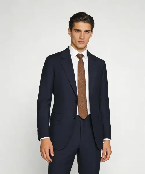 Costume bleu marine sur fond clair, veste droite à deux boutons avec revers classiques, chemise blanche et cravate brune à motif discret.