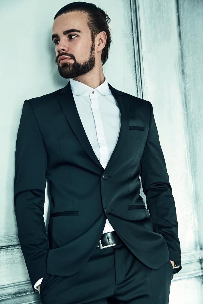 PureElegance : homme portant un costume noir sur mesure à la coupe ajustée, avec chemise blanche col classique, style sobre et élégant.