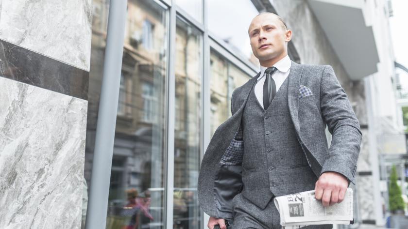 Tenue Pure Elegance : costume trois-pièces gris avec cravate noire et pochette, porté en extérieur devant des vitrines.