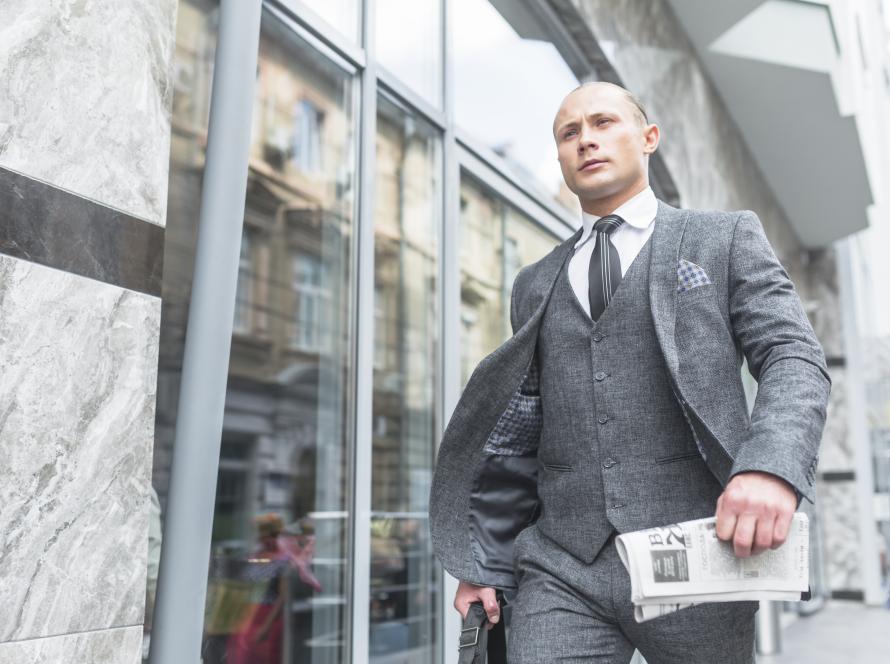 Tenue Pure Elegance : costume trois-pièces gris avec cravate noire et pochette, porté en extérieur devant des vitrines.