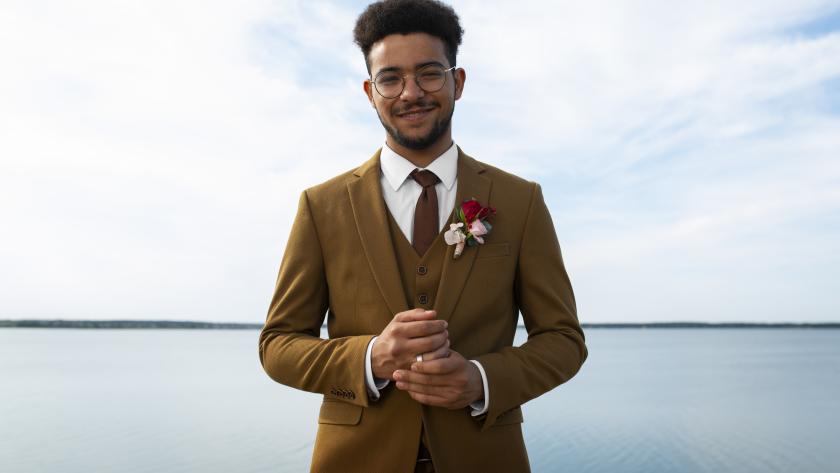 PureElegance : homme portant un costume camel 3 pièces sur mesure (veste, gilet, pantalon) avec chemise blanche, cravate assortie et boutonnière, style élégant cérémonie.