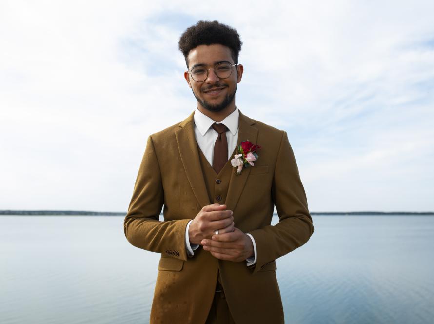 PureElegance : homme portant un costume camel 3 pièces sur mesure (veste, gilet, pantalon) avec chemise blanche, cravate assortie et boutonnière, style élégant cérémonie.