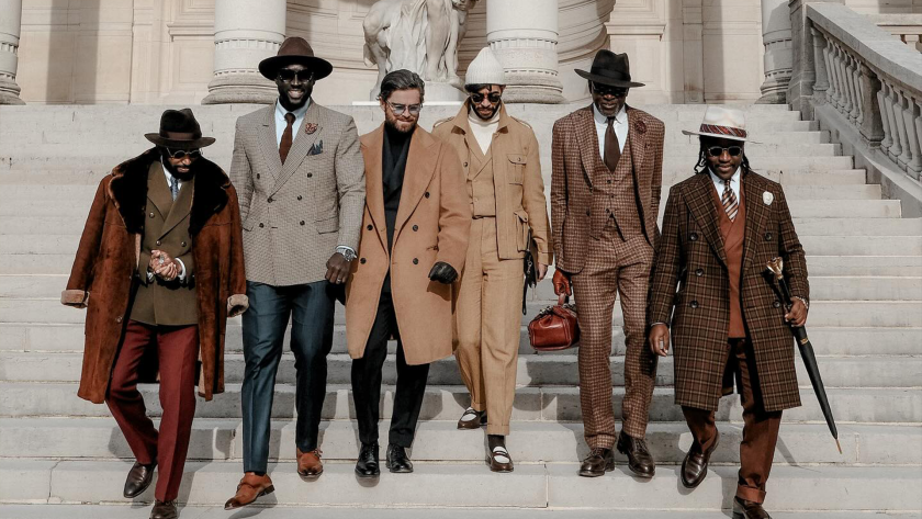 Groupe de six hommes descendant des marches d’un bâtiment classique, portant des tenues dandy vintage avec manteaux longs, costumes à carreaux, chapeaux et accessoires; tenues créées par Pure Elegance.