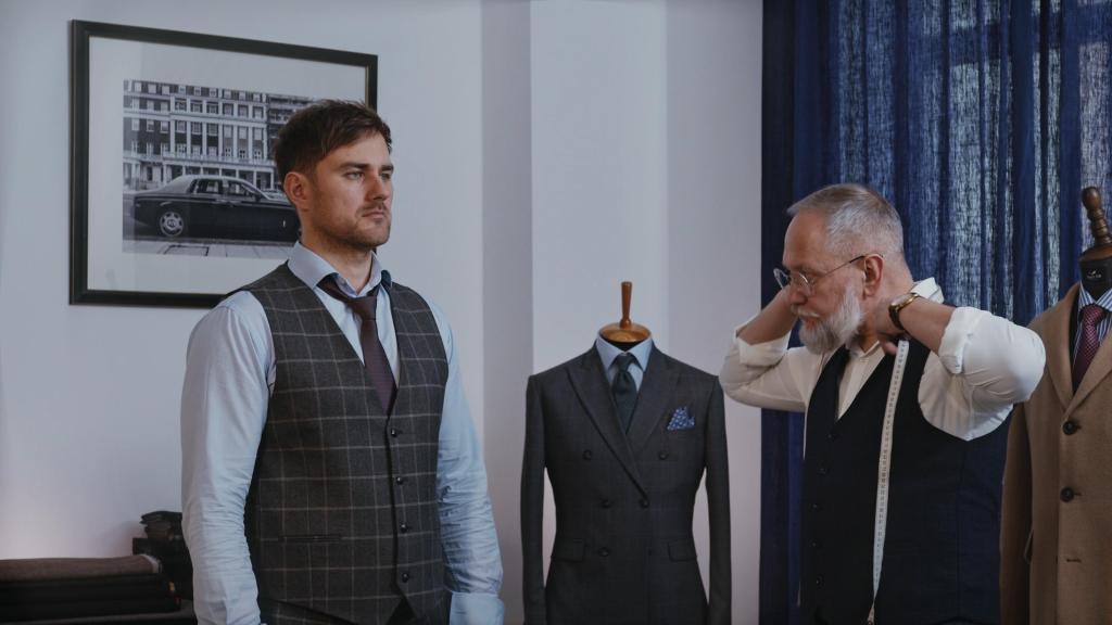 Essayage homme PureElegance avec gilet gris à carreaux, chemise bleu clair et cravate foncée.
